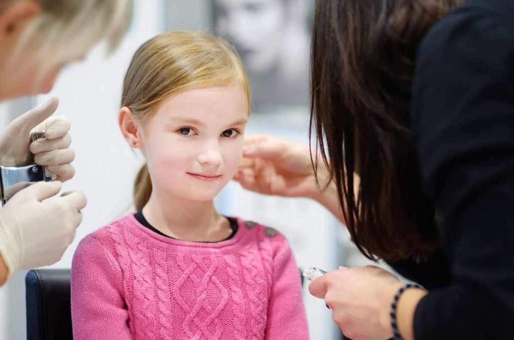 A woman puts a new earring in a little girl's ear