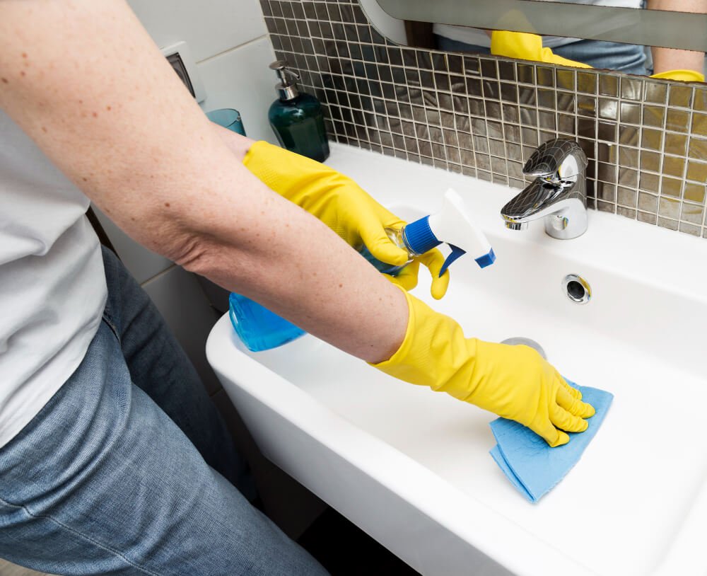 woman with rubber gloves cleaning sink